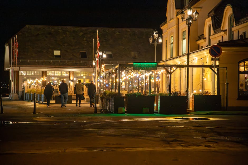 Vibrant night view of Ålesund's downtown with illuminated street restaurant and five people walking.