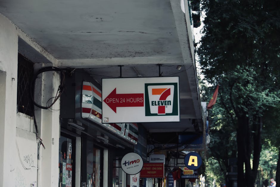 7-Eleven convenience store sign and storefront, open 24 hours in an urban setting.