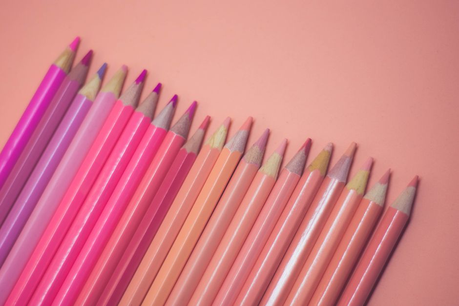 A collection of pink and pastel colored pencils laid on a soft pink background, offering a