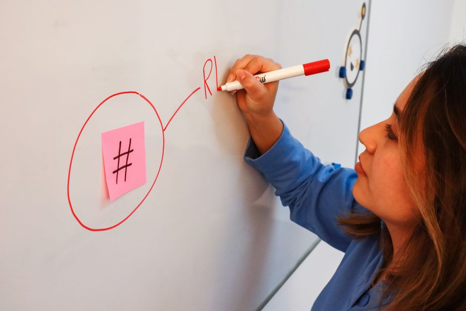 Focused woman writing on a whiteboard with marker, emphasizing hashtag concept.