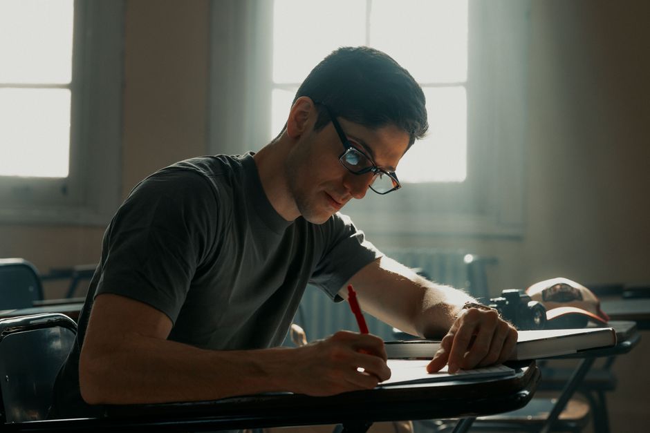 Focused university student studying in a sunlit classroom with a notebook and pen.