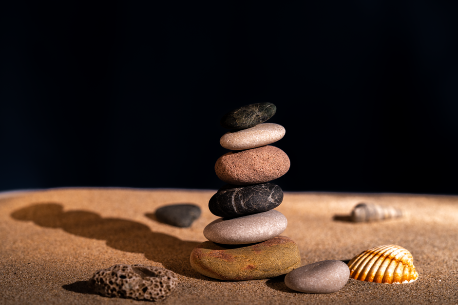 Artistic stack of smooth pebbles on sandy beach with seashells, capturing balance and zen.