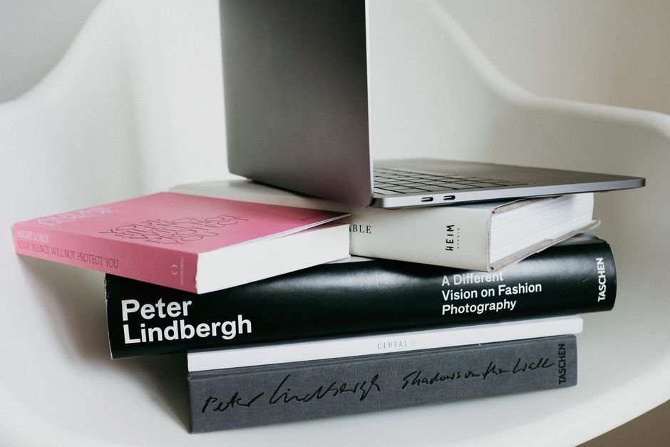 Gray portable netbook composed on stack of colorful art books from home collection on white chair in daylight