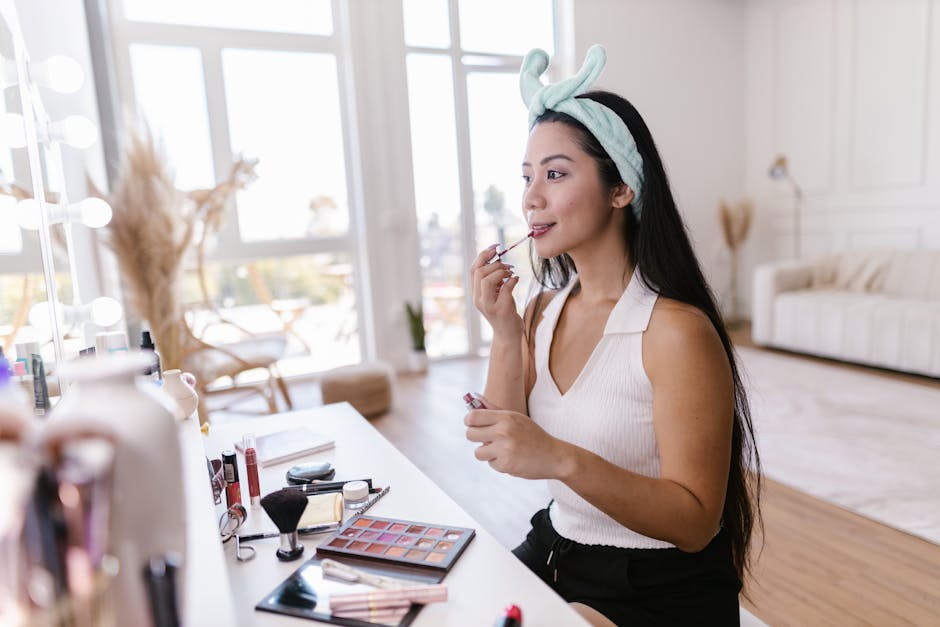 A woman in a white tank top applying makeup at a vanity in a stylish, bright room.