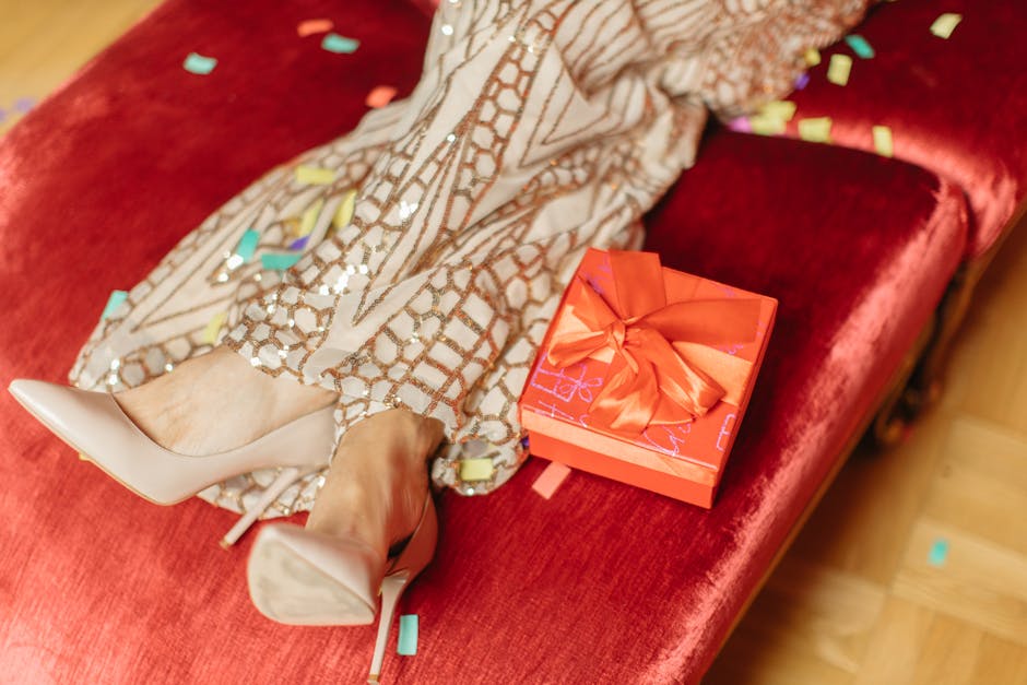 A stylish scene with high heels, a wrapped gift, and colorful confetti on a red sofa.