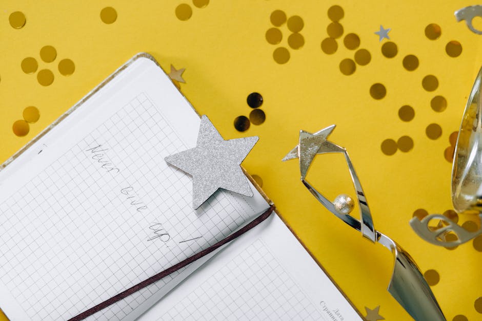 Flat lay of a notebook with motivational text, trophy, and star confetti on a yellow background.
