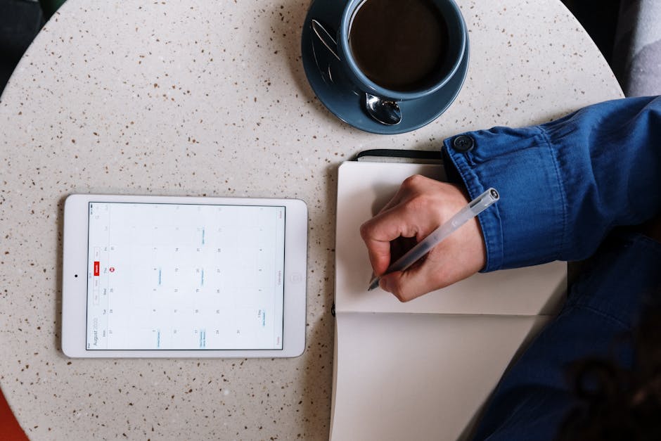 Overhead view of planning with a tablet, notebook, and coffee on a table.
