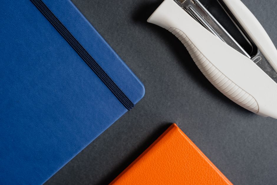 Blue and orange notebooks with a white stapler on a dark background.