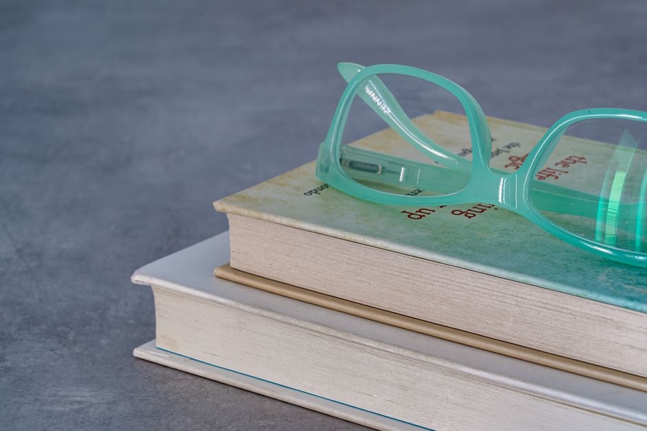 Close-up of stacked books with teal eyeglasses on top, perfect for reading themes.
