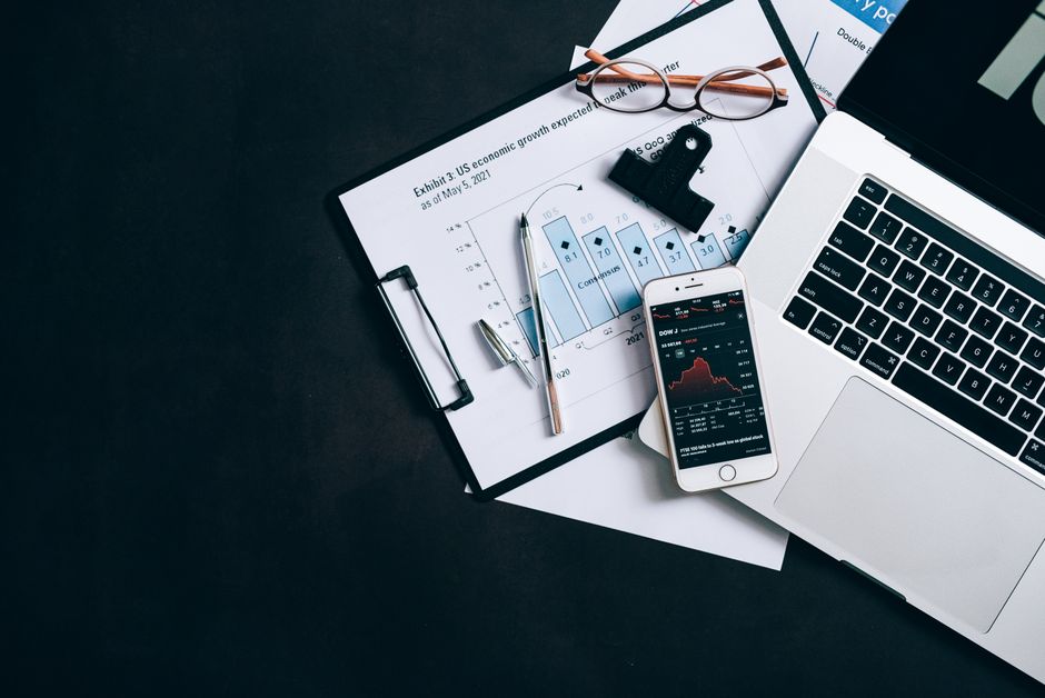 High angle view of an office desk with laptop, clipboard, and smartphone displaying stock market data.