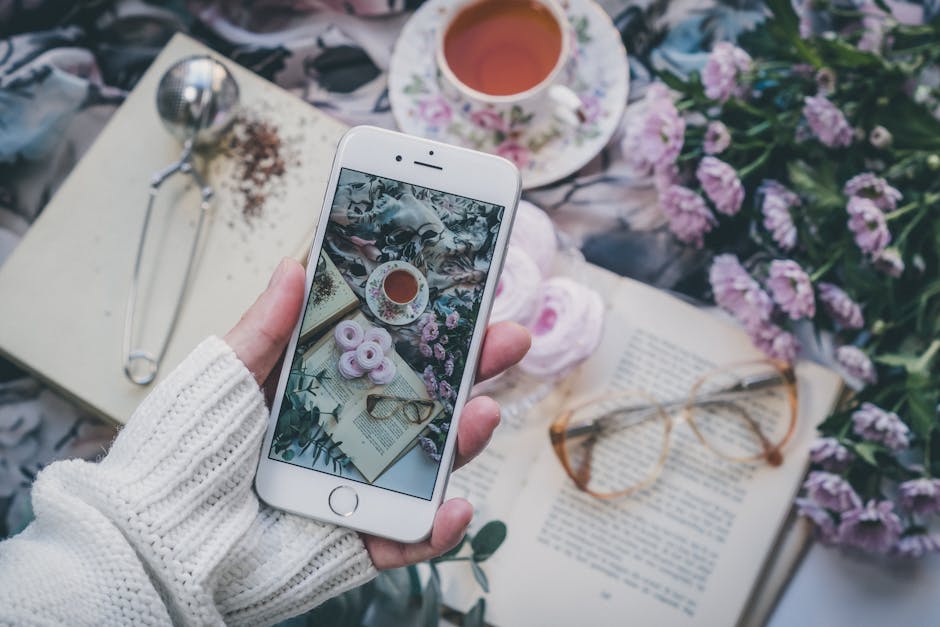 Flat lay with cup of tea, flowers, and smartphone reflecting a cozy vibe.