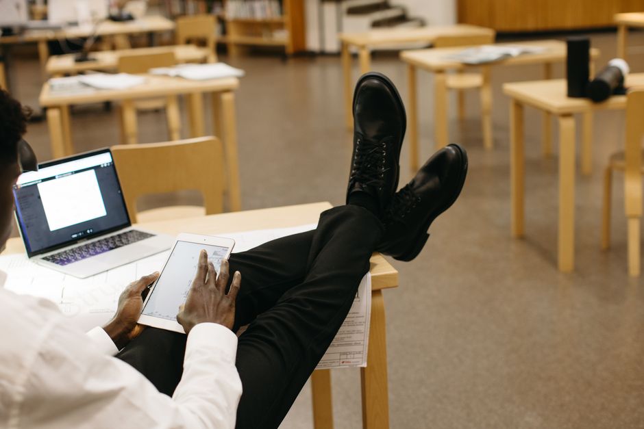 Professional using tablet and laptop in a relaxed office setting with crossed legs.