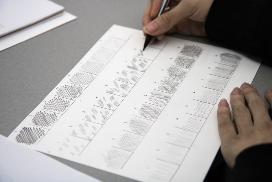 Close-up photo of hands using a pen to practice shading techniques on paper.