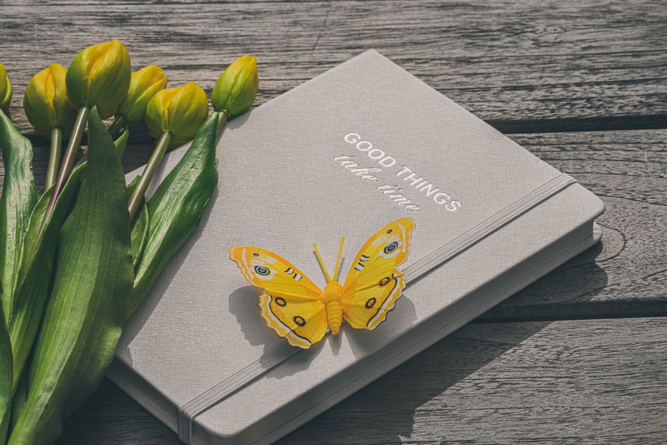 A yellow butterfly rests on a notebook with tulips, capturing a serene and inspirational moment.