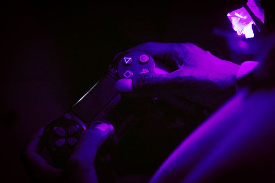 A close-up shot of hands gripping a gaming controller, illuminated by purple light, creating a vibrant atmosphere.