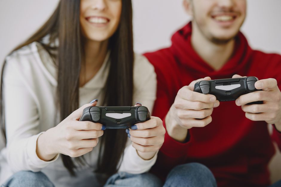 From below of unrecognizable positive male and female in casual wear smiling and playing video game while using gamepads and sitting in living room