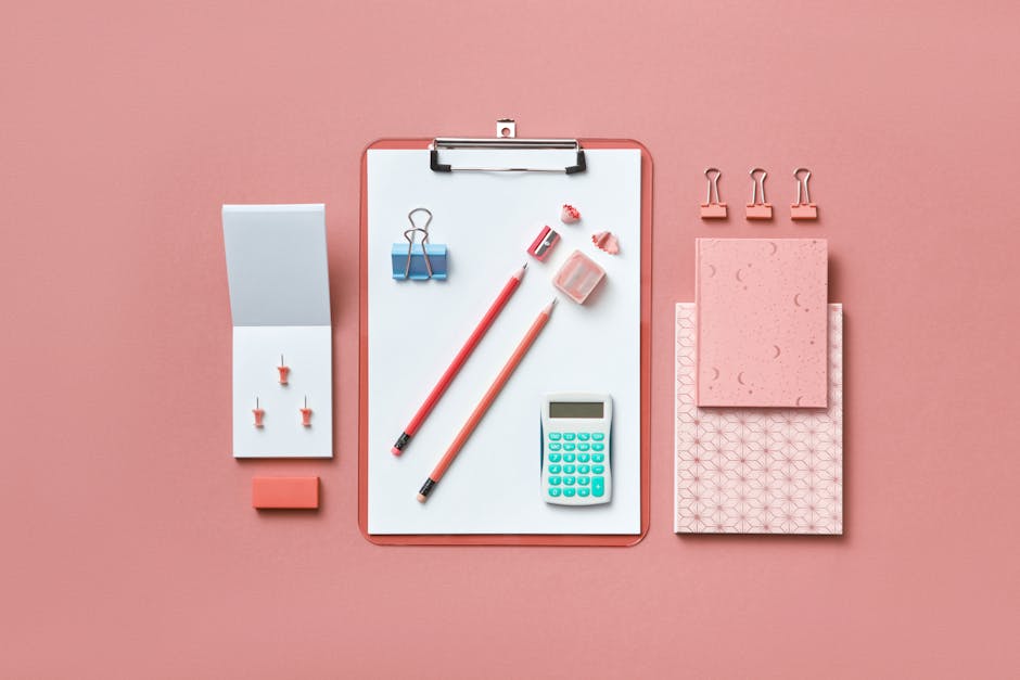 A modern flat lay of various office supplies arranged neatly on a pink background.