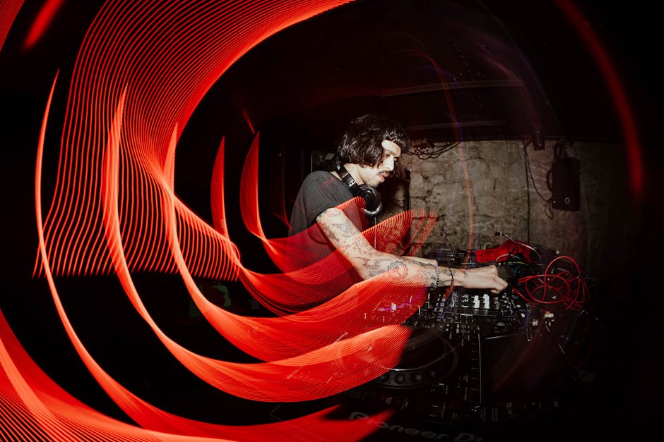 A DJ performing in a dimly lit club with captivating red light trails and mixing equipment.