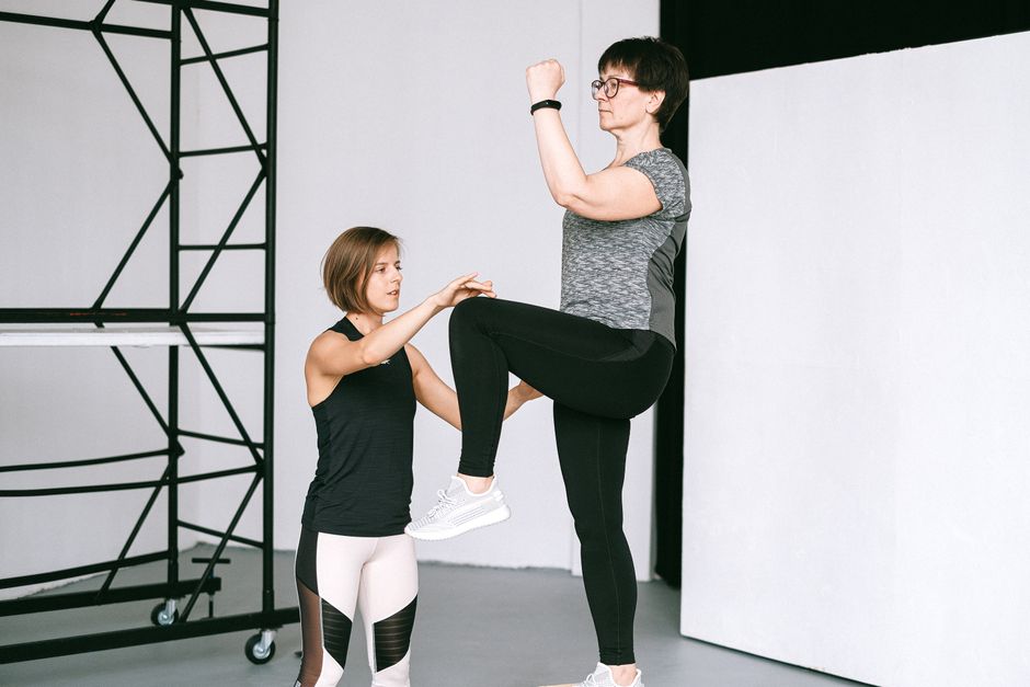 An elderly woman performs exercises with a fitness coach, focusing on a healthy lifestyle and wellness indoors.