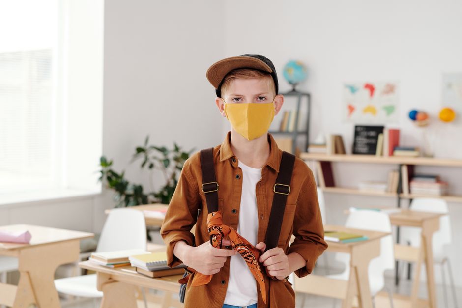Boy wearing a face mask and backpack in a modern classroom, adapting to new normal school environment.