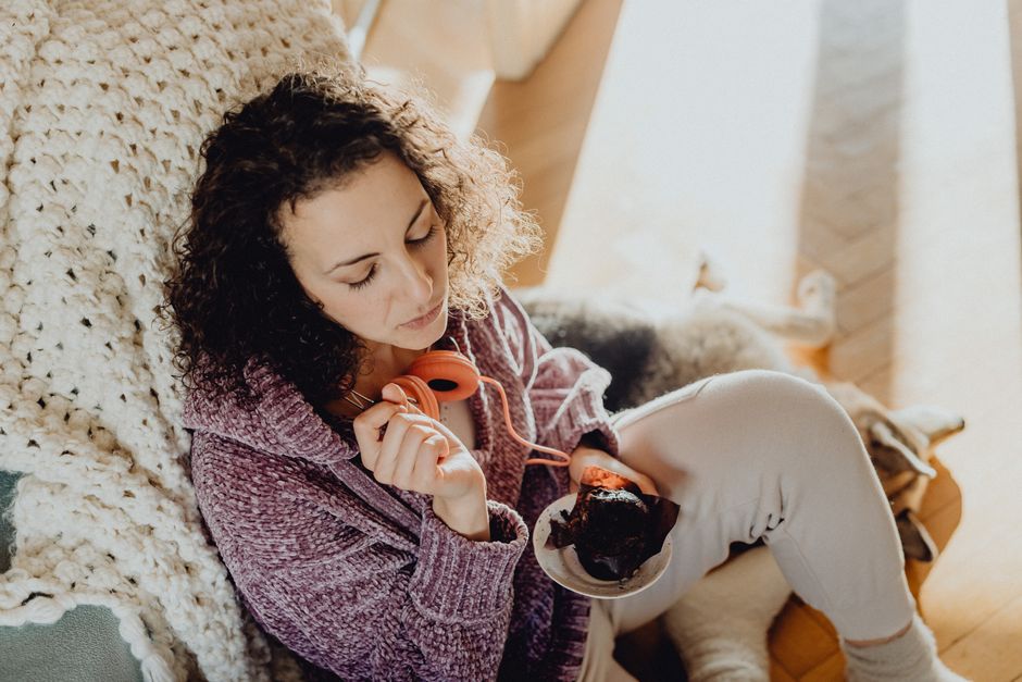Woman in casual clothes enjoys dessert and music at home, exuding relaxation.
