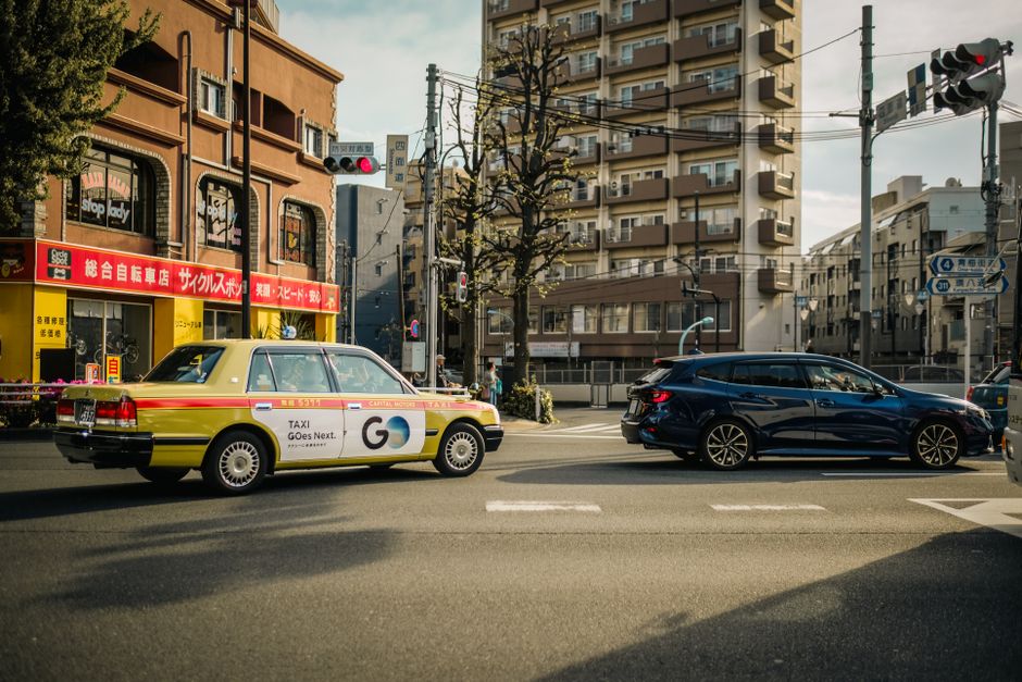 A city street featuring a traditional taxi and a modern vehicle under clear skies.