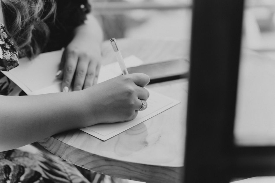 Black and white image of a person writing on paper at a table, emphasizing creativity.