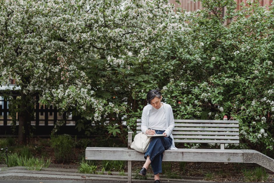 Woman sketching on a bench surrounded by blossoming trees in a peaceful park.