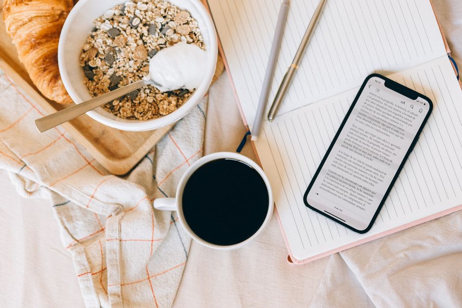 Top view of breakfast with croissant, cereal, coffee, and phone on notebook.