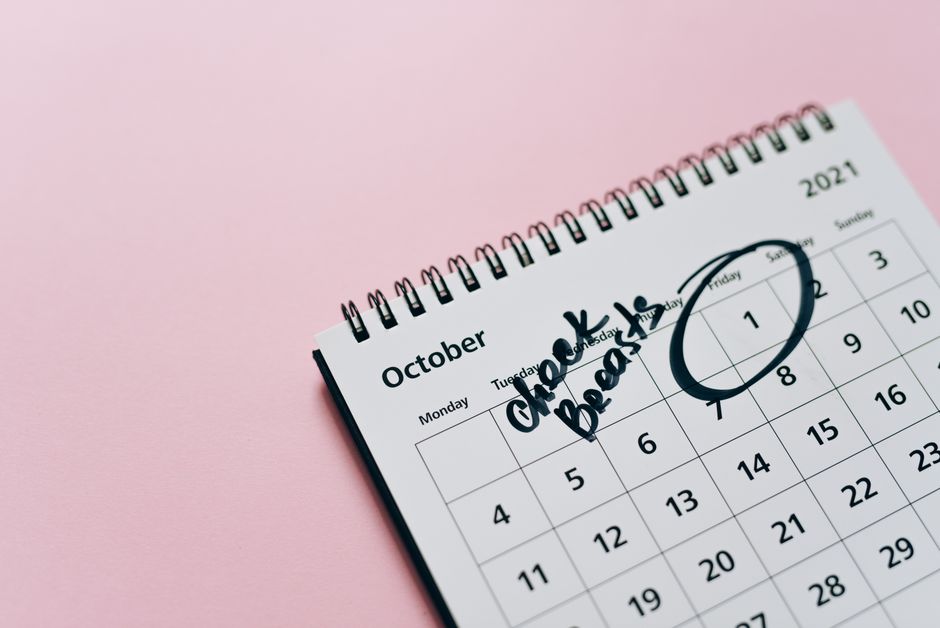 October calendar with breast check reminder, emphasizing health awareness on a pink backgr