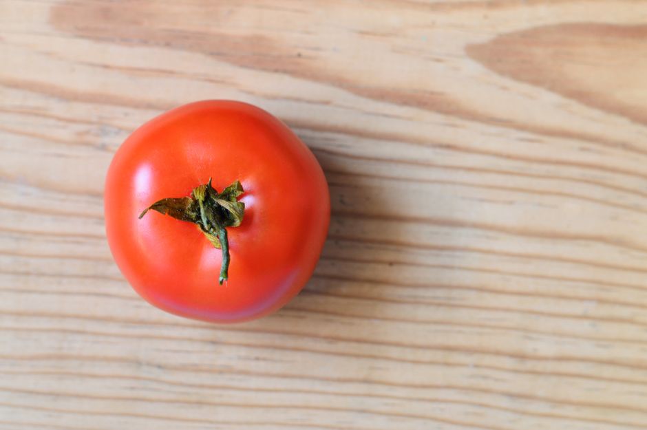 A fresh red tomato placed on a natural wooden surface viewed from above.