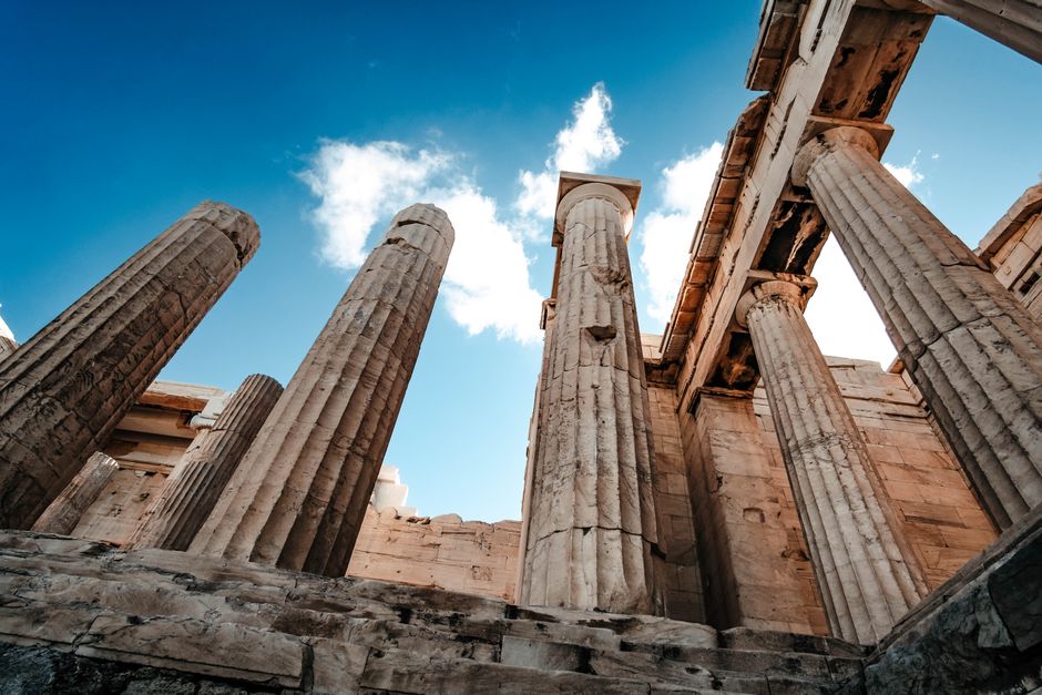 A low-angle view of the ancient columns at the Acropolis in Athens, Greece, against a bright sky.