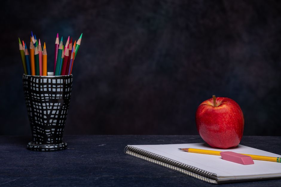 Set of multicolored pencils in cup holder placed on table with eraser on copybook and ripe
