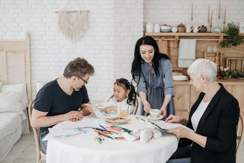 A joyful family with an adopted girl sitting and interacting at a table in a cozy home setting.