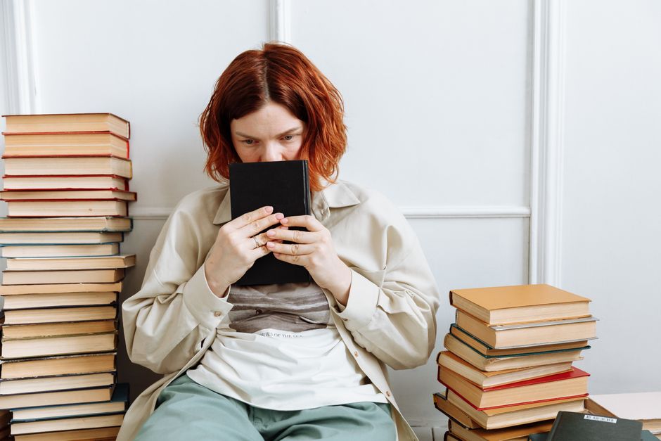 Woman sitting with a book surrounded by stacks of books, deep in thought.