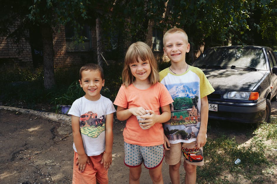 Three smiling children stand together outdoors on a sunny day, exuding joy and friendship.