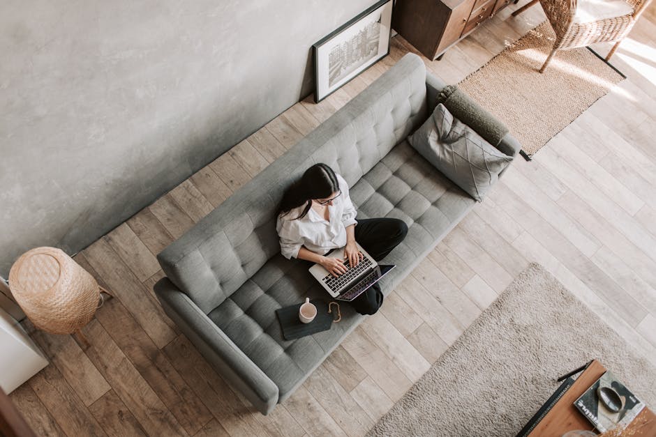 High angle view of a woman working on a laptop while sitting on a sofa in a modern living room.